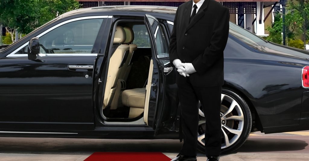 Limo driver standing next to opened car door with red carpet